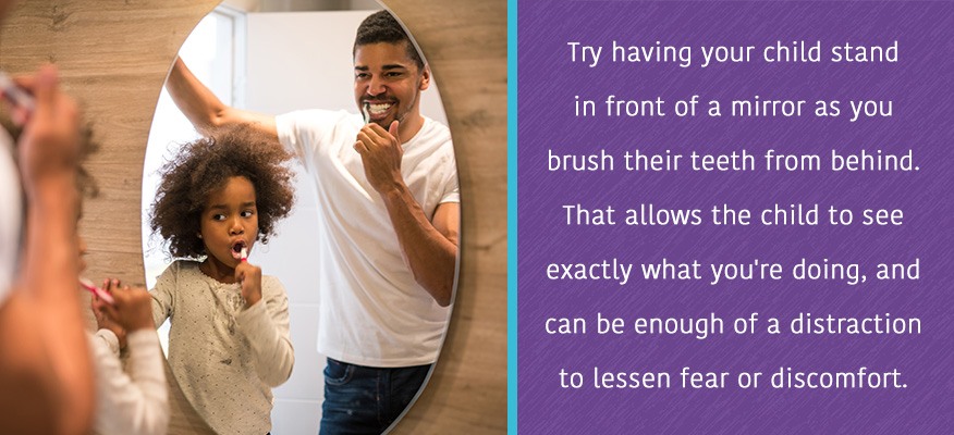 Try having your child stand in front of a mirror as you brush their teeth from behind. 