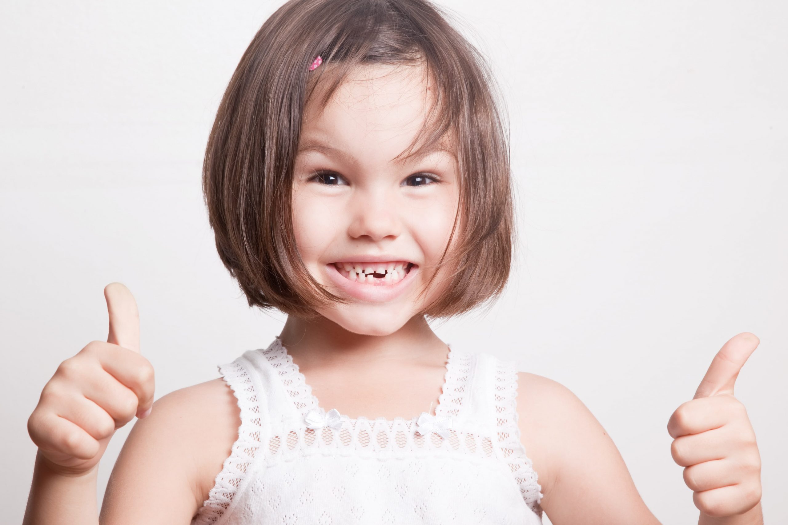 little girl with missing front teeth smiles with two thumbs up